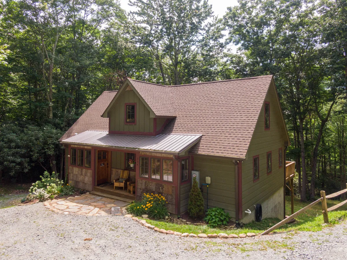 The charming front porch with wooden seating, flower beds, and a stone path showcases inviting entryways and a seamless connection to the natural landscape. The porch is ideal for greeting the morning sun or watching snowfall, reinforcing the lodge’s welcoming, homey atmosphere in every season.