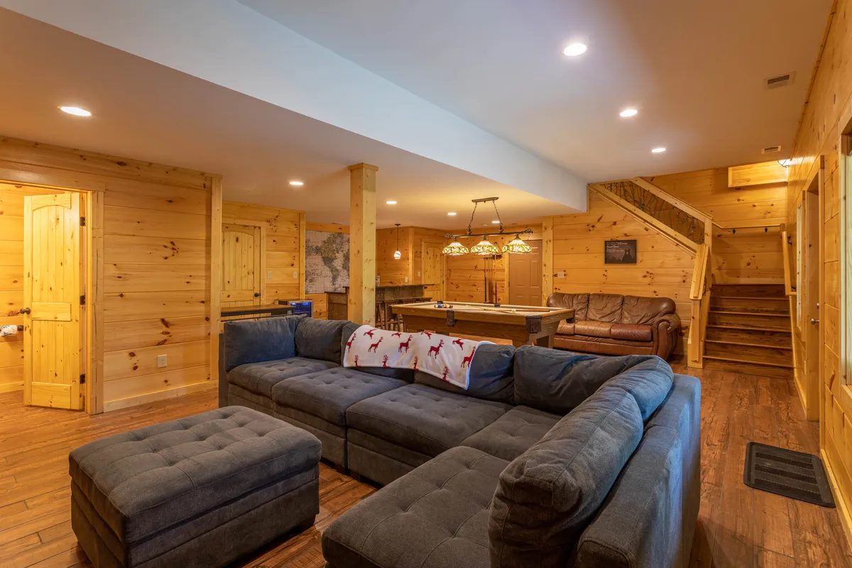 Featuring a spacious sectional sofa, a wooden staircase, a dining area with pendant lights, and a prominent wall map, this image suggests a multi-purpose lounge ideal for movie marathons, casual dining, and group relaxation.