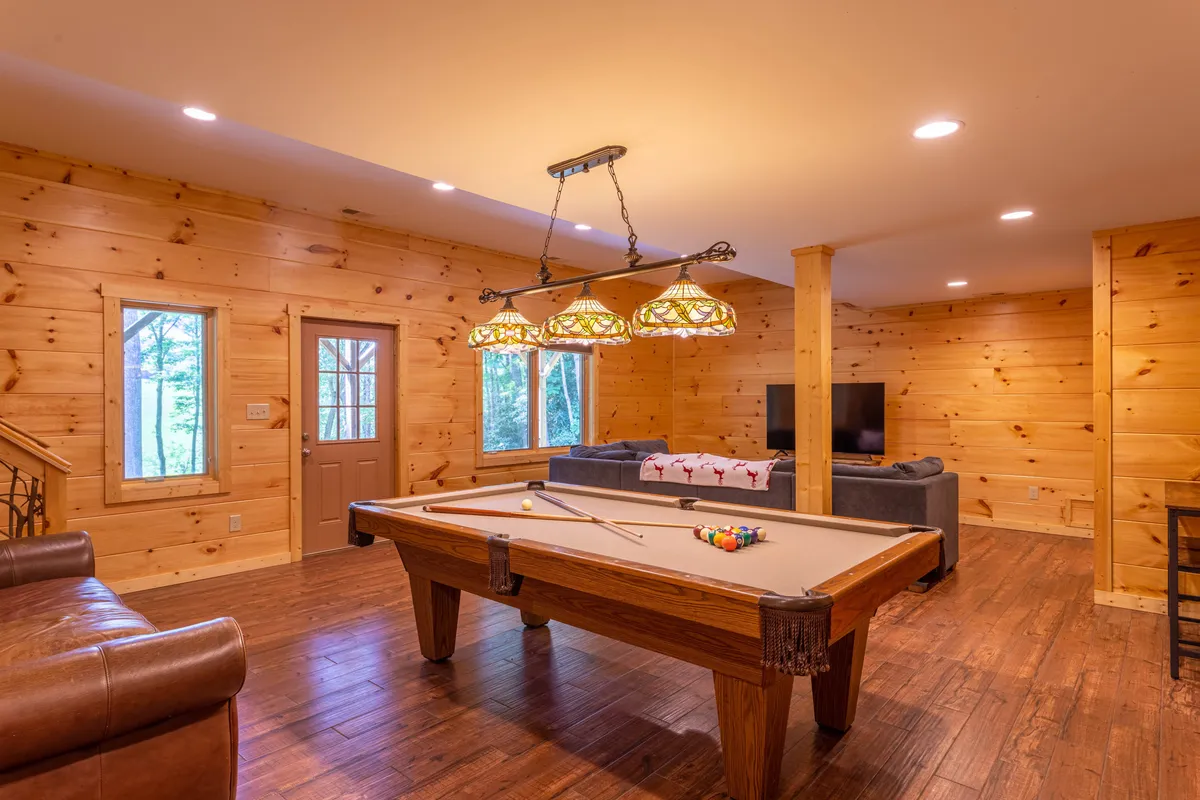 This image centers on a pool table positioned under stained glass light fixtures, with a comfortable seating area nearby. The layout exudes a fun, social atmosphere ideal for friendly games and group gatherings—exactly the vibe described for the entertainment room.