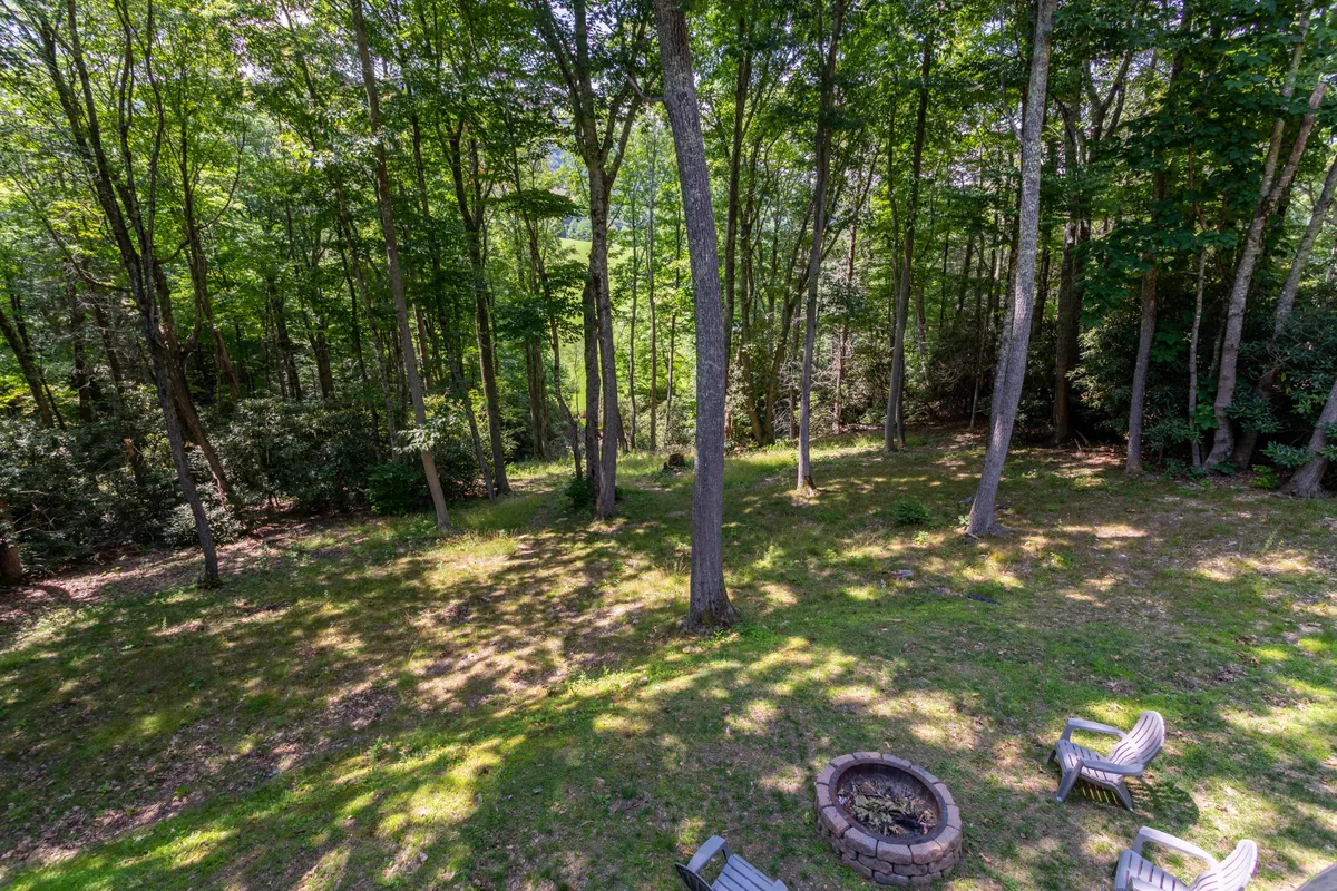 An inviting woodland fire pit area surrounded by comfortable seating, nestled in a wooded setting. The arrangement suggests welcoming gatherings, storytelling, and evenings spent under the stars, with the forest providing a peaceful and private ambiance.