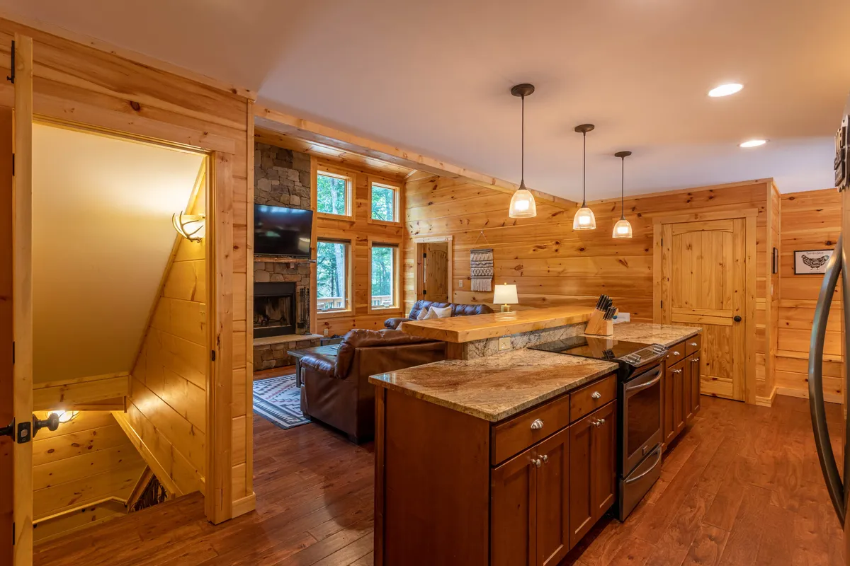 An open-concept space where the kitchen island, seating area, fireplace, and large windows coexist harmoniously. The arrangement encourages cooking, entertaining, and relaxing together, with mountains visible beyond.
