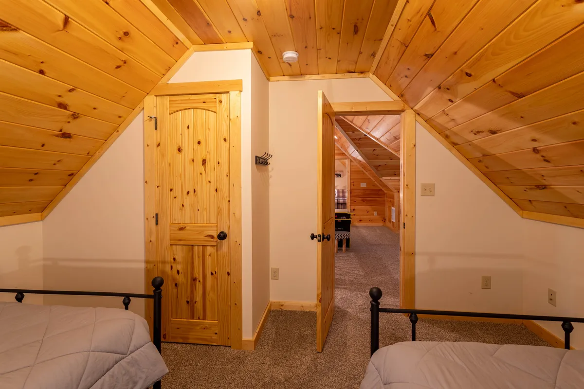 A loft space featuring angled wooden ceilings, two light-bedded sleeping areas, and wooden doors. The setting is bright and inviting, offering an airy nook for reading or quiet relaxation away from the main living areas.