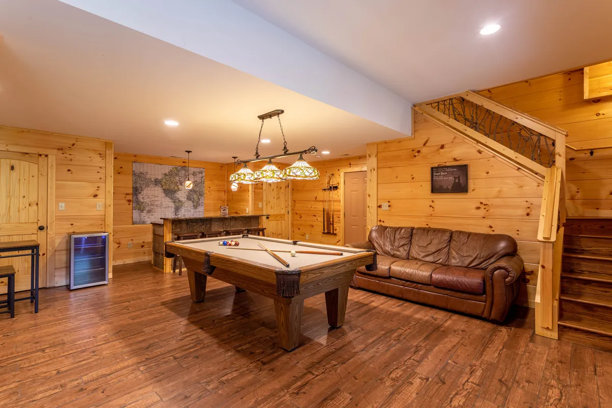 A spacious downstairs entertainment room with a pool table as the centerpiece, complemented by a leather couch and a map on the wall. The setting feels lively yet comfortable, offering a place for friendly competition and relaxed family gatherings indoors.